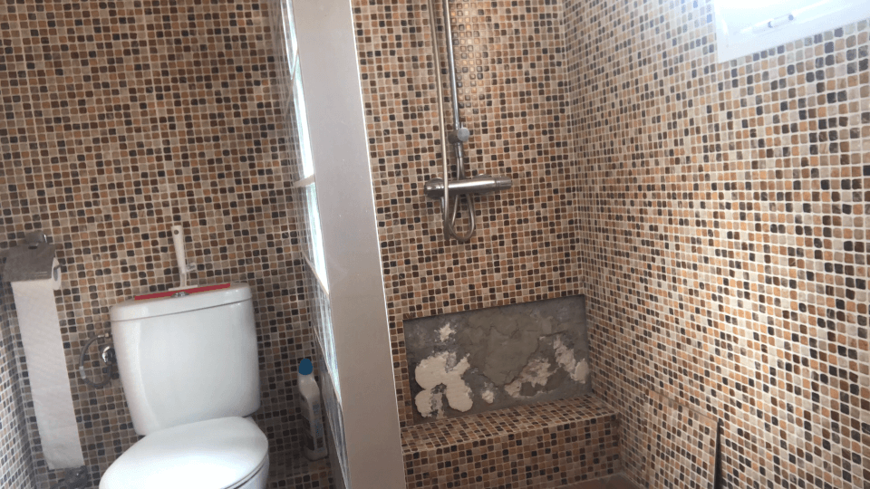 This image features a handyman from Handyman Aguilas working on fixing bathroom wall tiles. The technician is focused on carefully removing damaged tiles and installing new ones to achieve a flawless finish