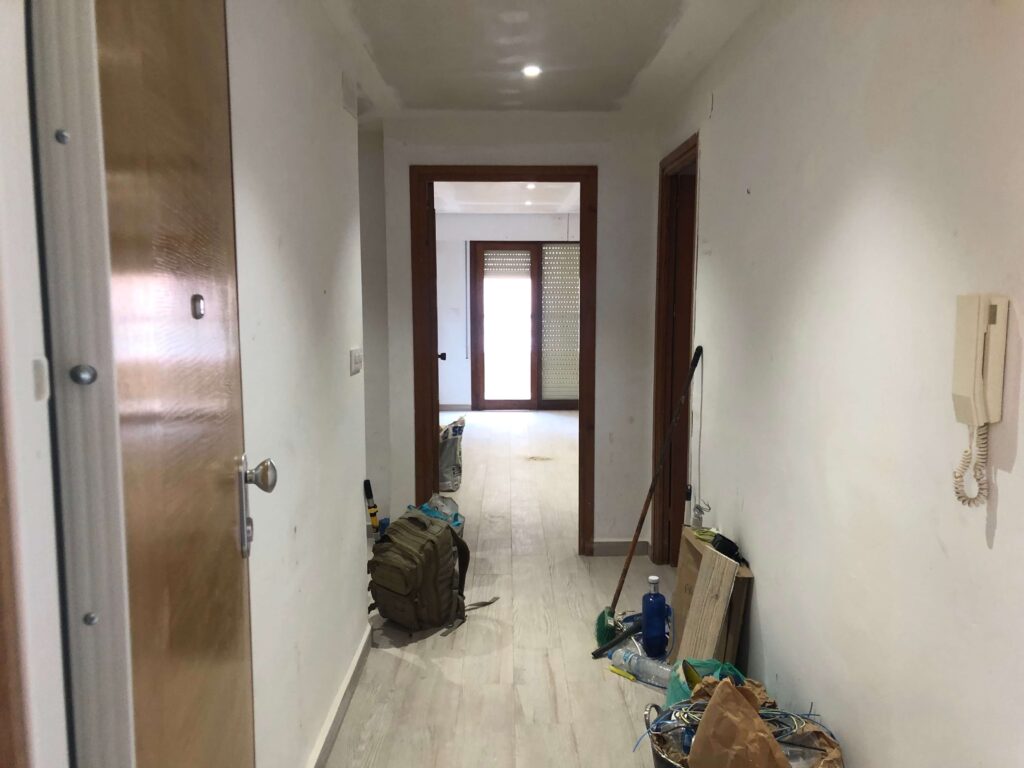 Imagen de un piso preparado y listo para pintar:
"Piso preparado para pintar con las paredes parcheadas y alisadas, cinta de pintor aplicada a lo largo de los bordes y molduras, y los muebles cubiertos con sábanas protectoras, asegurando un espacio de trabajo limpio y organizado"