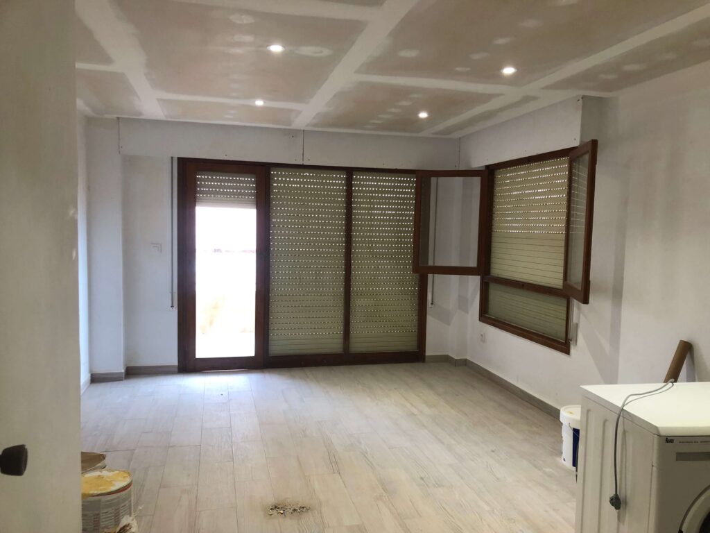 Image of a flat prepped and ready for painting:
"Flat prepped for painting with walls patched and smoothed, painter's tape applied along the edges and trim, and furniture covered with protective sheets, ensuring a clean and organized workspace."